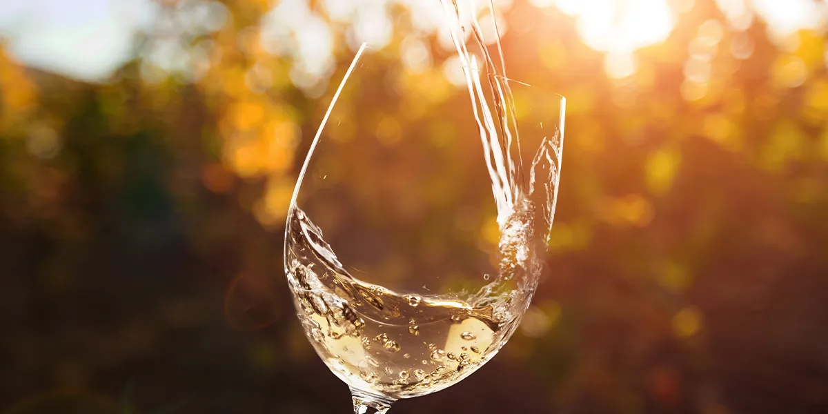 White wine being poured into a glass in golden sunlight, symbolising last bank holiday drinks 2025 celebrations