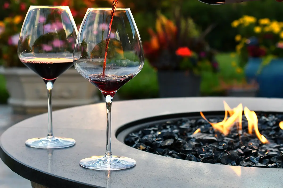 Red wine being poured into glasses beside a glowing firepit, perfect for Alfresco Night Drinks
