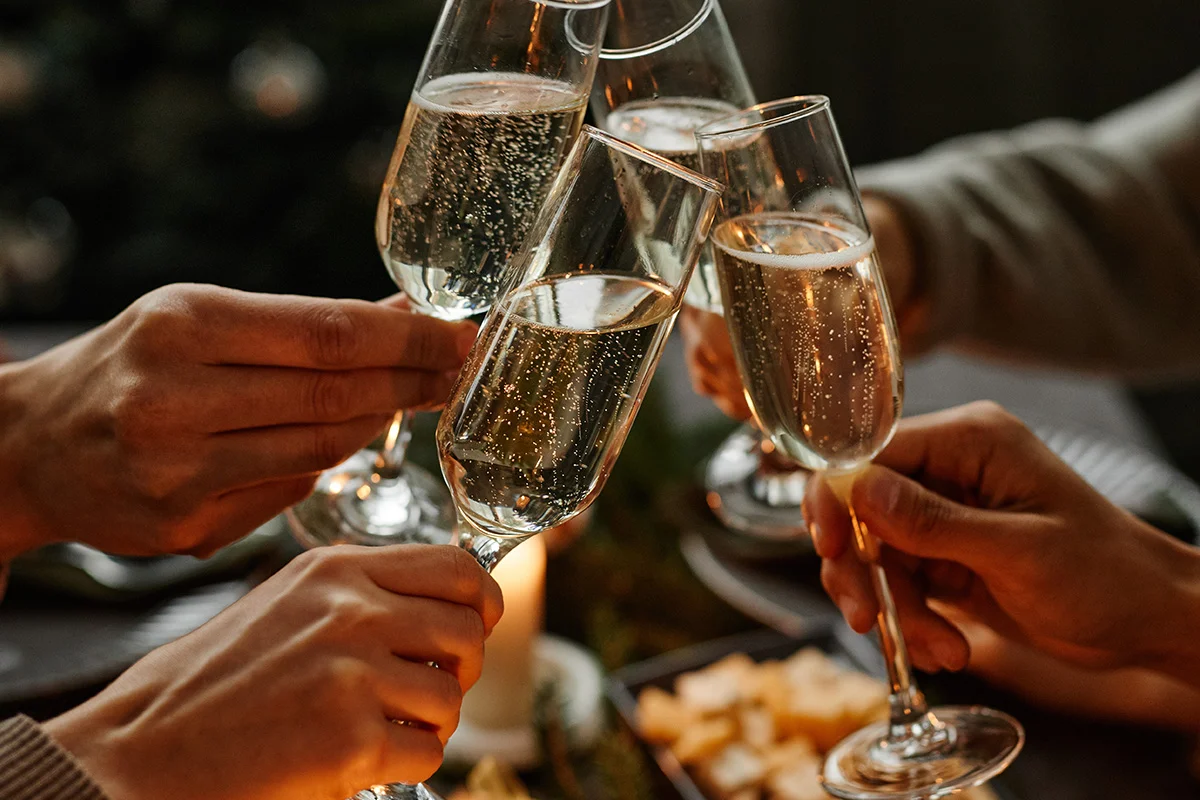 Friends toasting Champagne flutes at a festive dinner table, celebrating with Wine Rack’s Christmas drinks deals near you