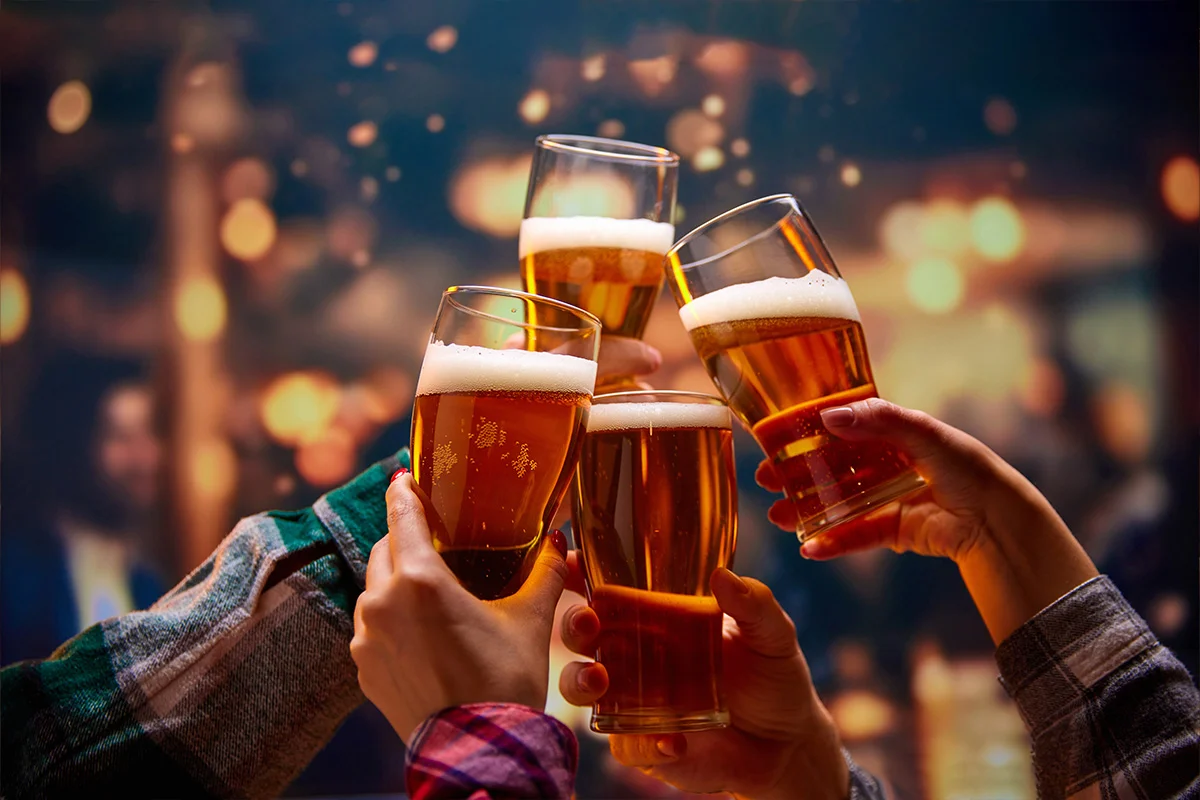 Friends raising pints of golden beer in a warm festive setting, celebrating with Wine Rack’s Christmas drinks deals near you