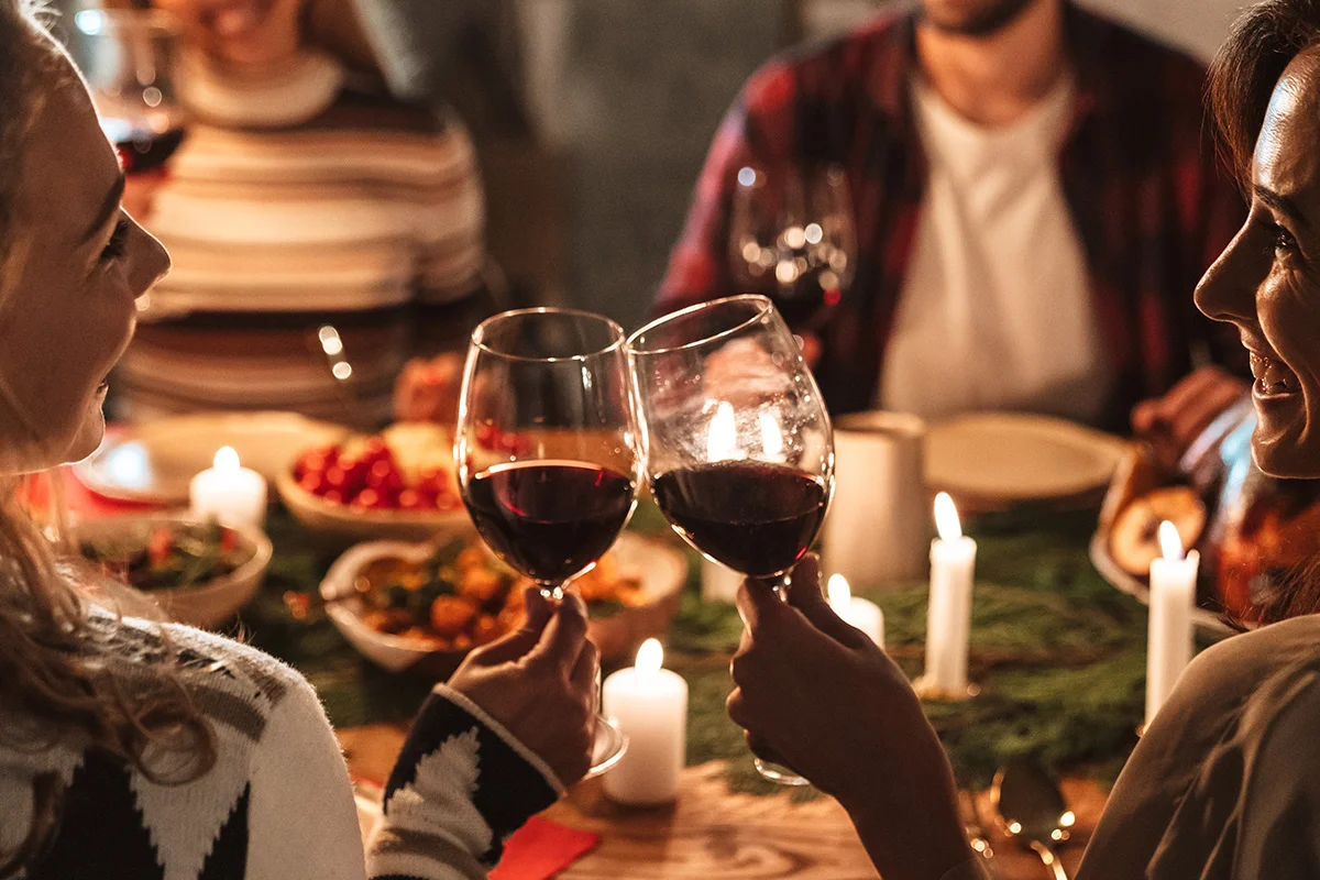 Friends toasting glasses of red wine over a candlelit festive dinner, showcasing Wine Rack’s Christmas drinks deals near you