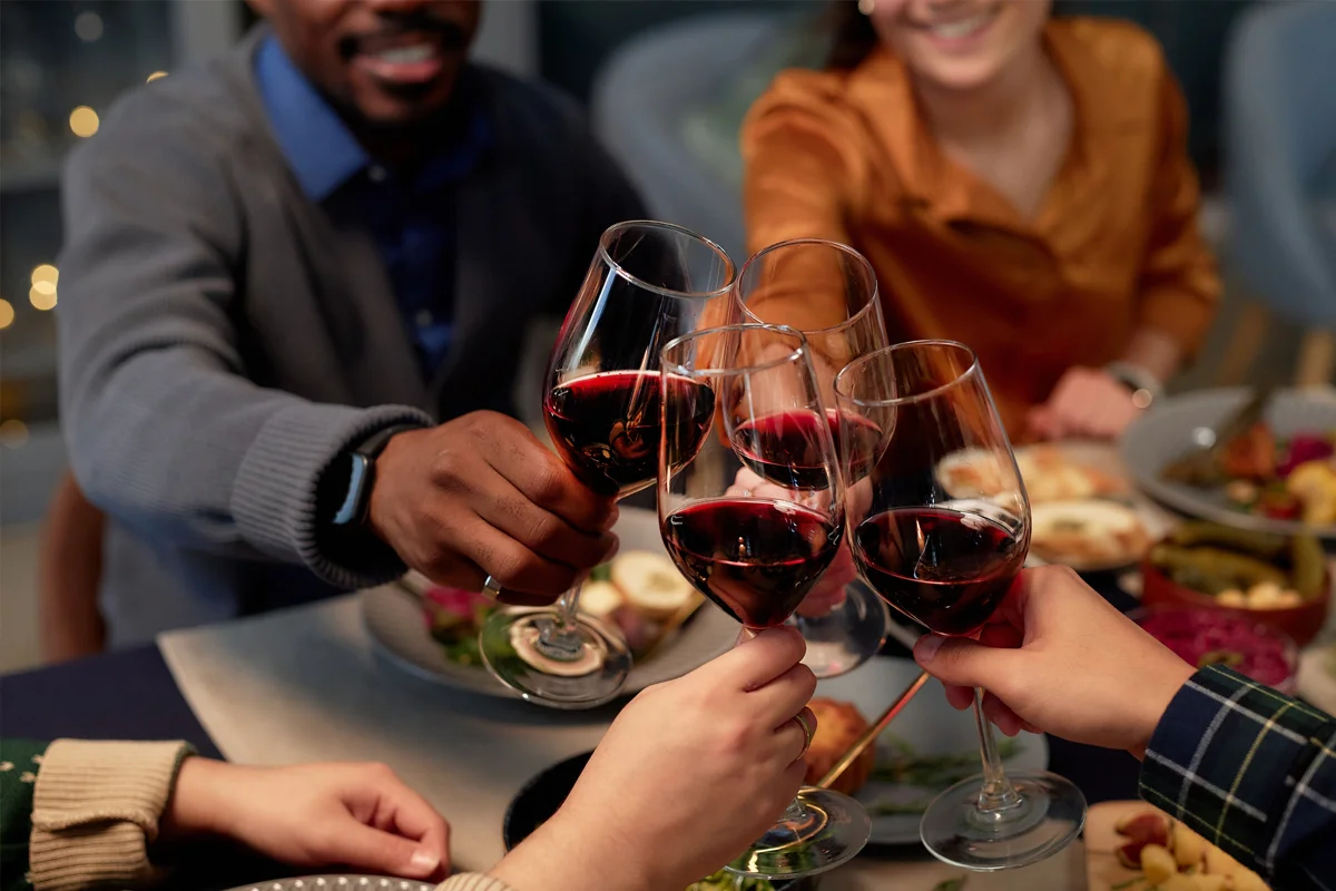 Friends clinking glasses of red wine over a festive dinner table with plates of food.
